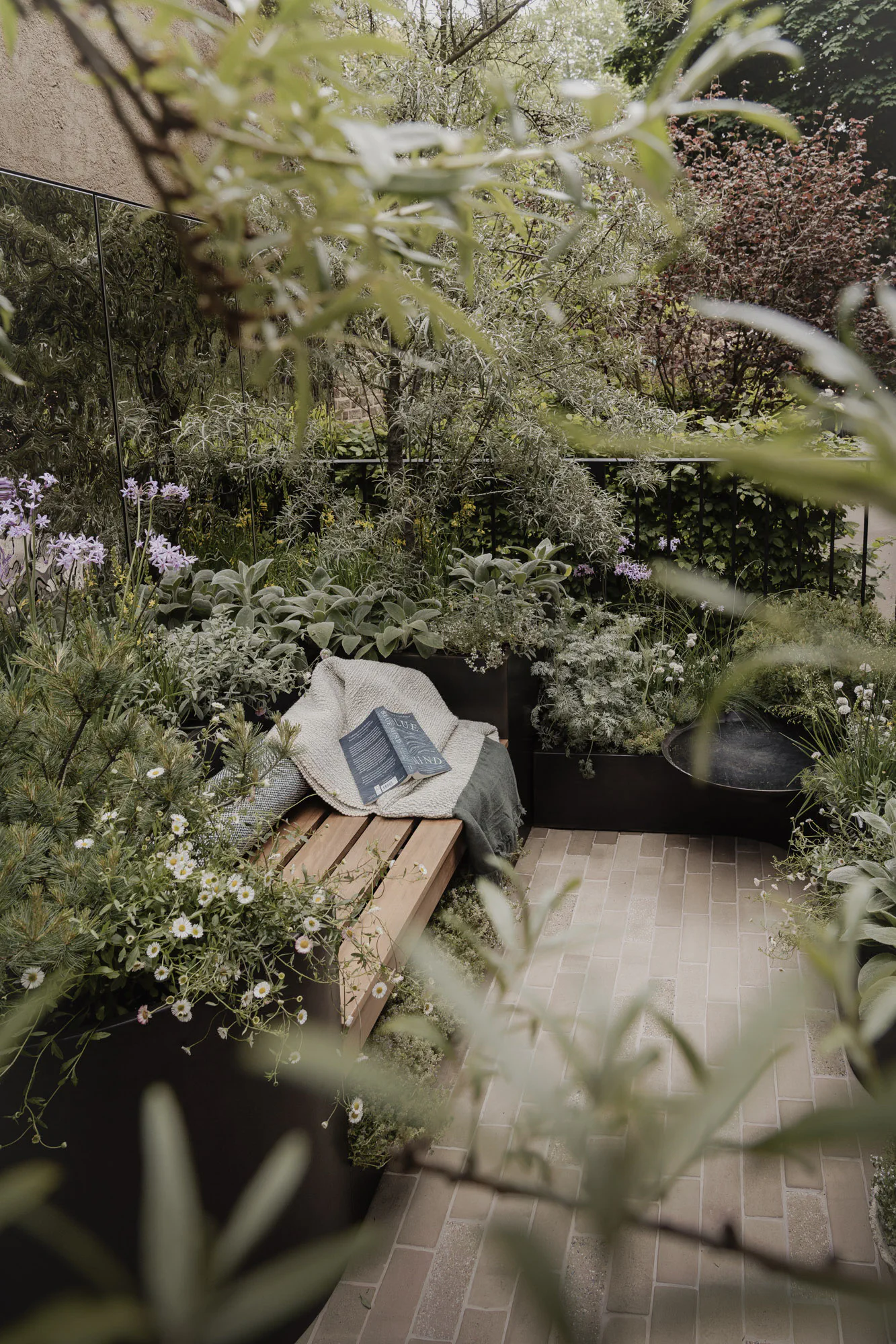 Timber bench with a blanket and book, surrounded by soft silvery planting on the balcony