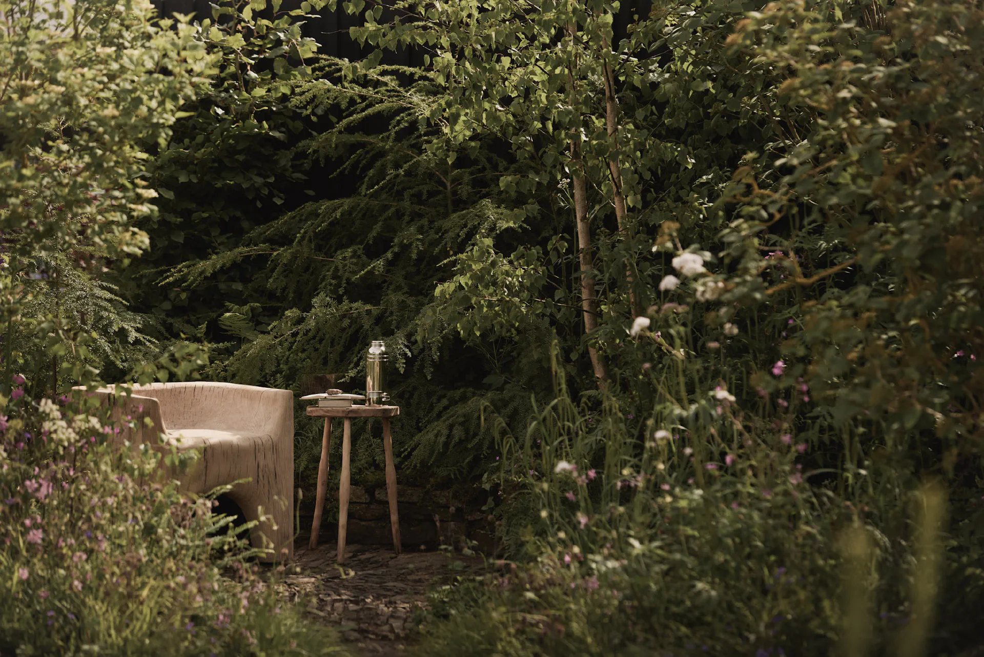 A pale upholstered chair and wooden side table in a clearing beneath conifers